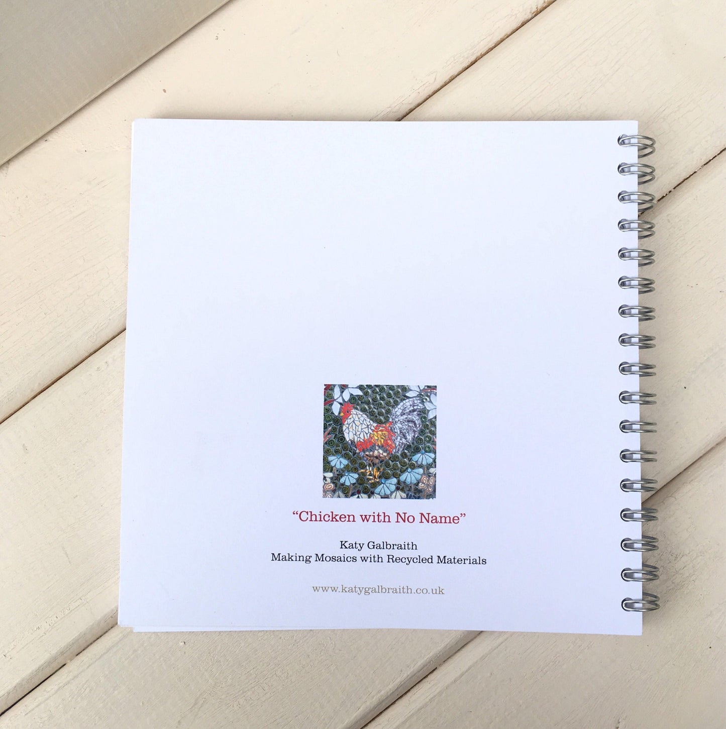 reverse side ofa spiral bound notebook, which is mostly white but has a small image and artist details
