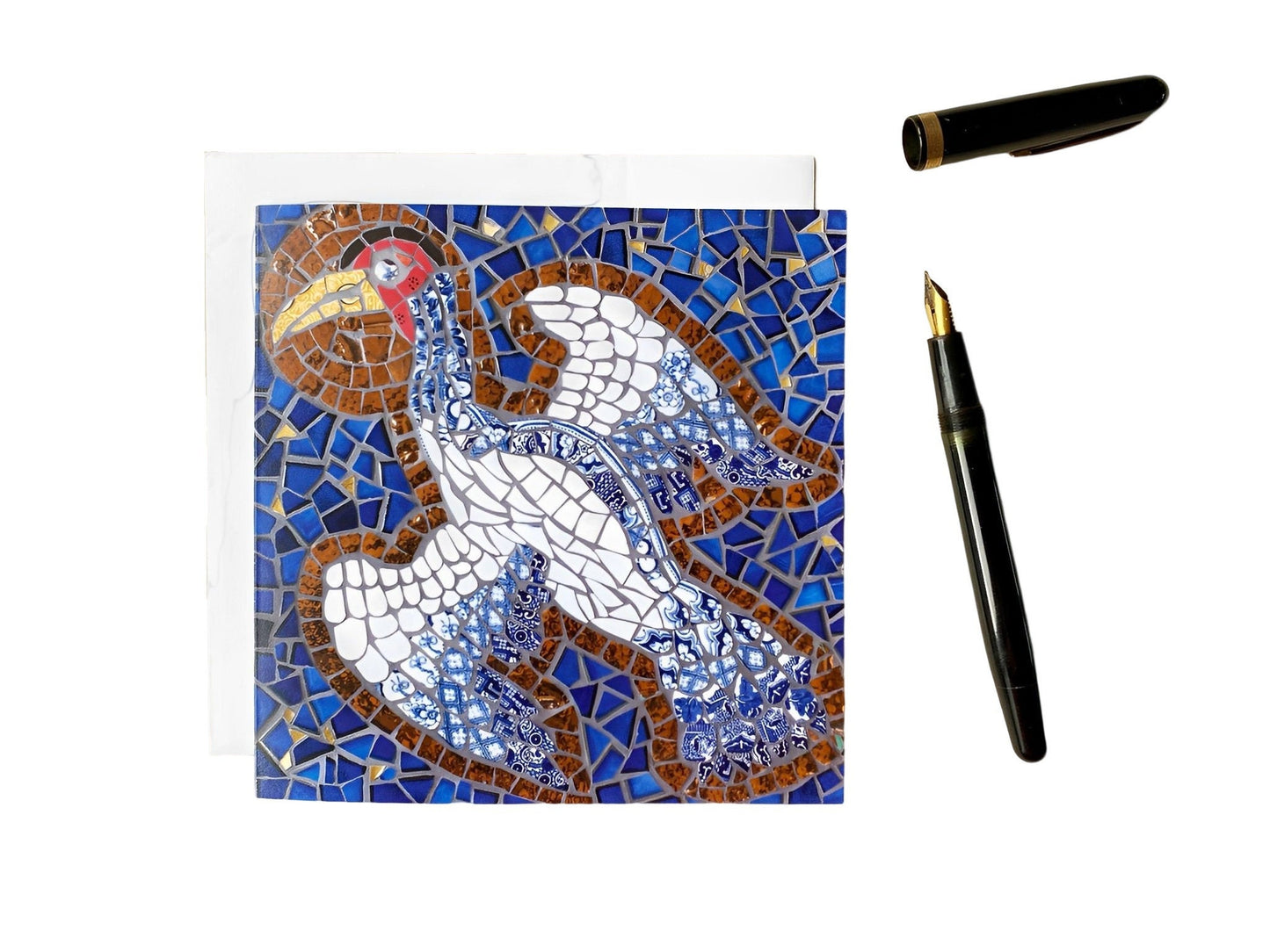 a square card with a crane bird with a halo depicted in mosaic. blue tile background. The bird has a white body and the tail & wing feathers are in blue and white traditional china. Photographed with a white background and an ink pen alongside