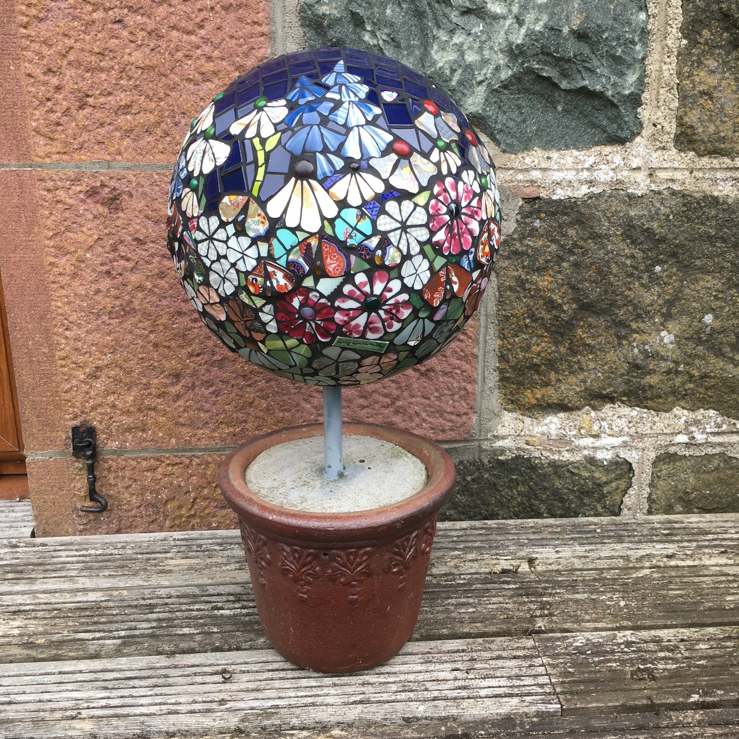 a big ball with a pole into a garden pot. The ball is covered with mosaic depicting a garden of flowers