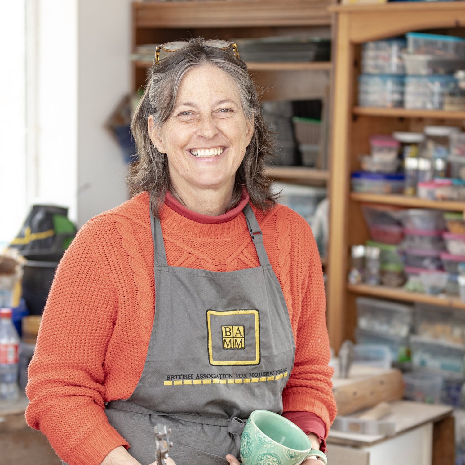 female with orange jumper and apron on, with mosaic storage in the background