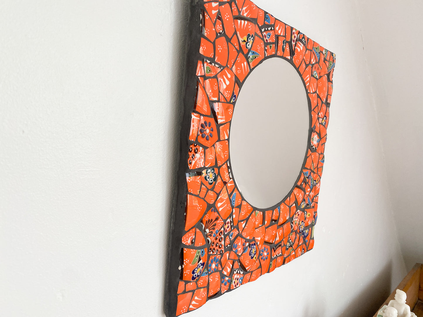 Bright orange mosaic mirror made from Turkish pottery. Square in shape with a circular mirror. Photographed on a wall