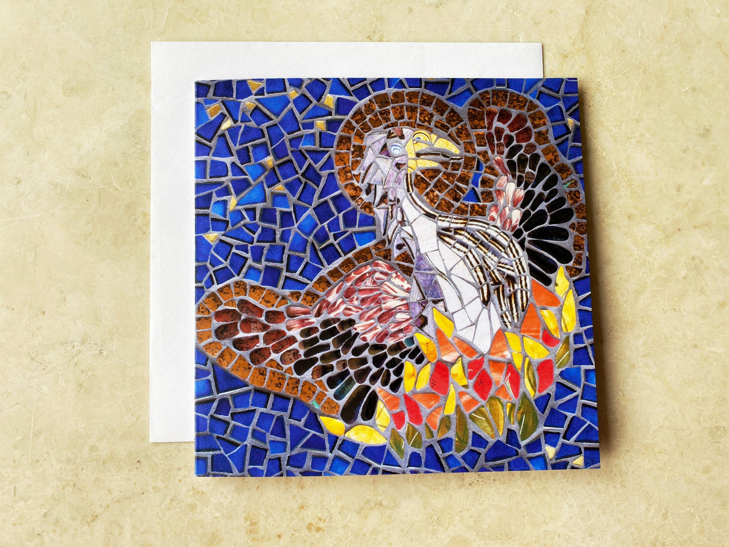 The Phoenix bird rising from the ashes with a halo depicted in mosaic. Dark blue tile and gold background. The bird has a brown body and wings and the fire is in oranges, yellows and red tiles. Photographed on a neutral background