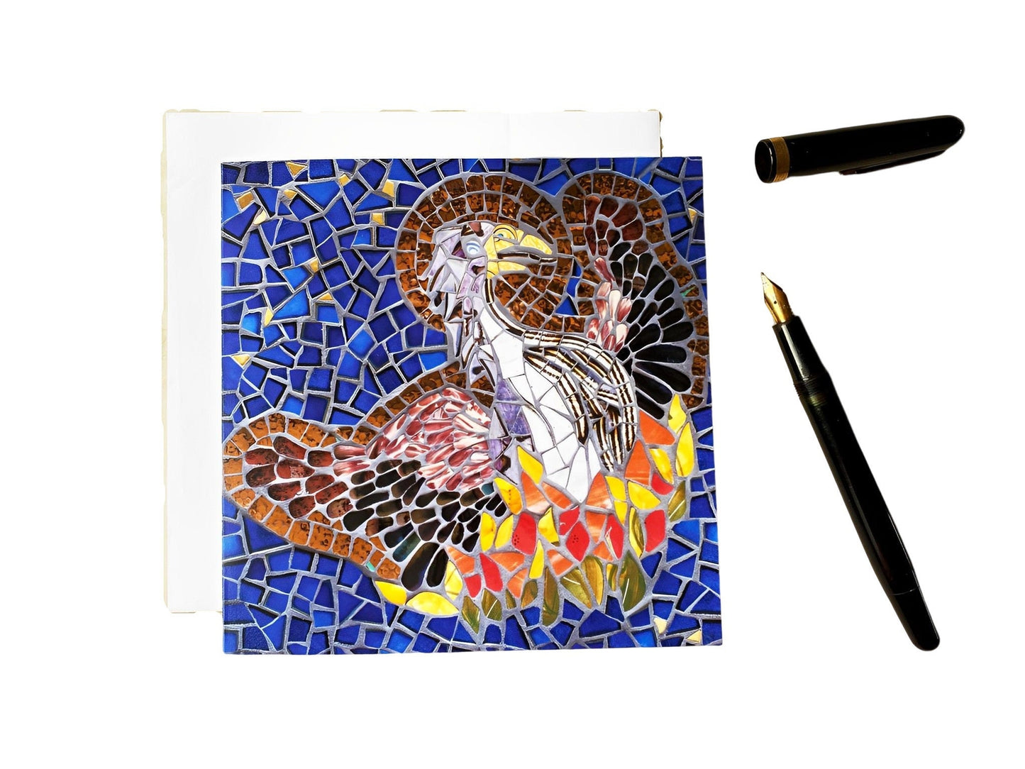 The Phoenix bird rising from the ashes with a halo depicted in mosaic. Dark blue tile and gold background. The bird has a brown body and wings and the fire is in oranges, yellows and red tiles. Photographed on a white background with an ink pen alongside.