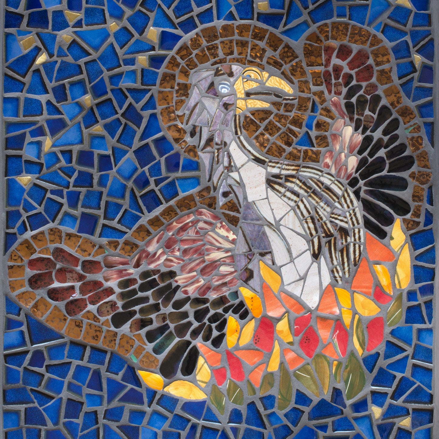 Phoenix bird rising from the ashes with a halo depicted in mosaic. Dark blue tile and gold background. The bird has a brown body and wings and the fire is in oranges, yellows and red tiles