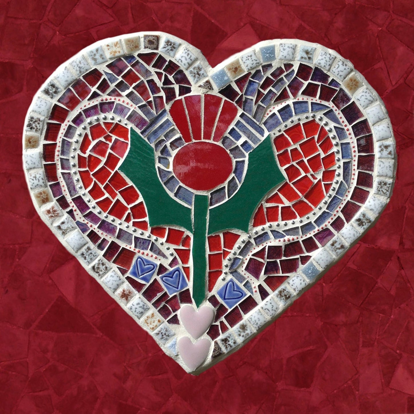 A square card with a thistle on a heart shape, in a mosaic pattern, with a red background.