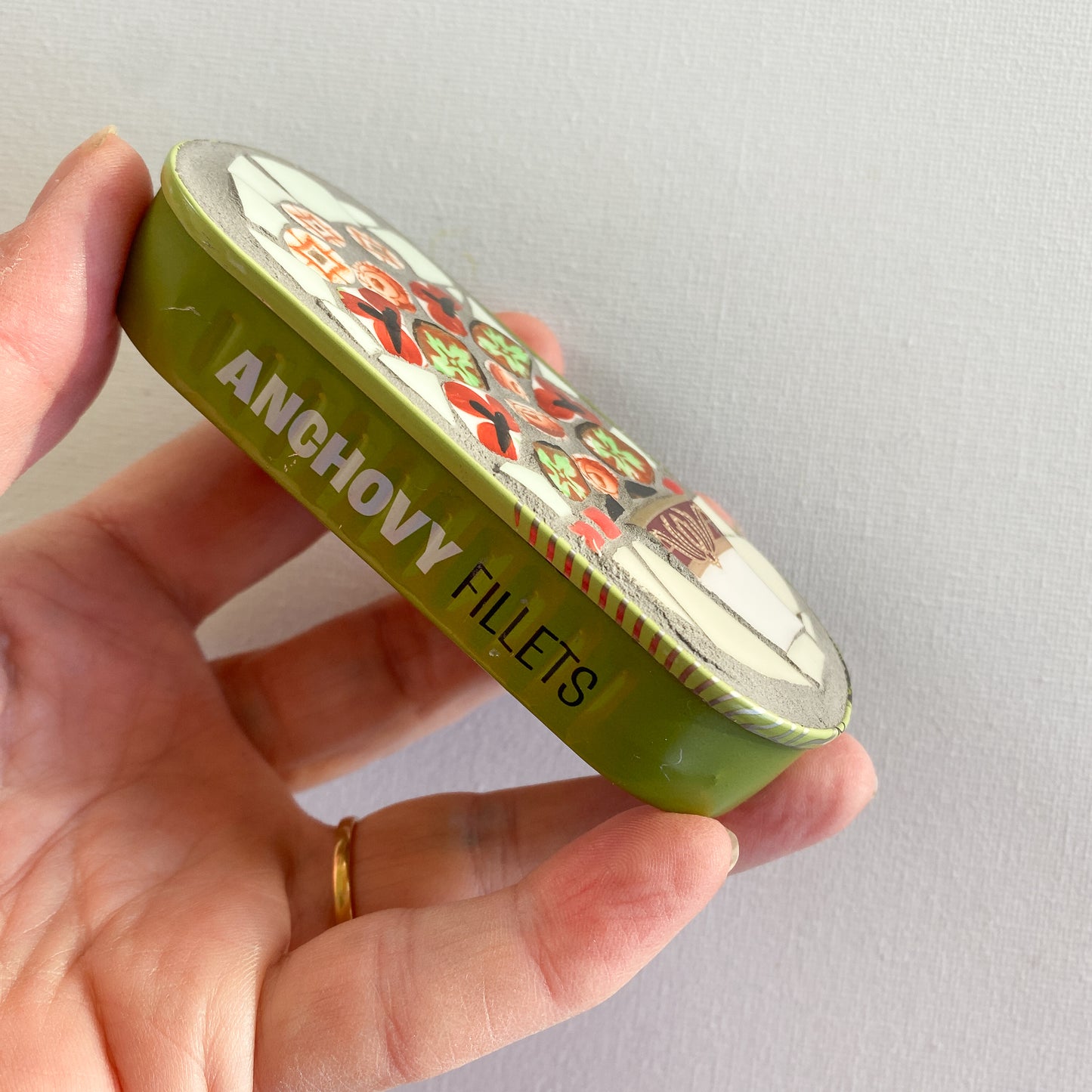 Hand holding a mosaic made in an anchovy can with a plain background