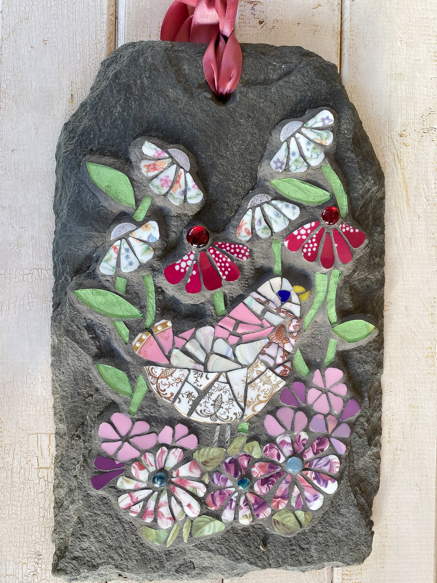 mosaic on slate of a pink gold and white bird surrounded by mosaic flowers in pink, hot pink and chintz tones. leaves in pale green glass