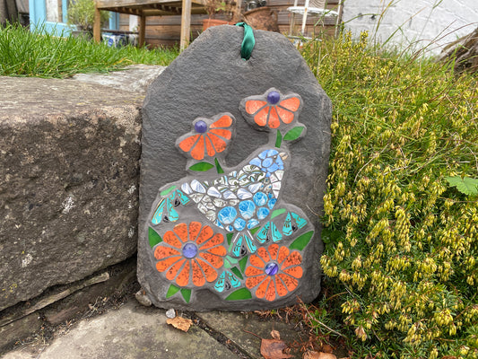 Decorative slate with mosaic design of a bird and flowers in a garden setting