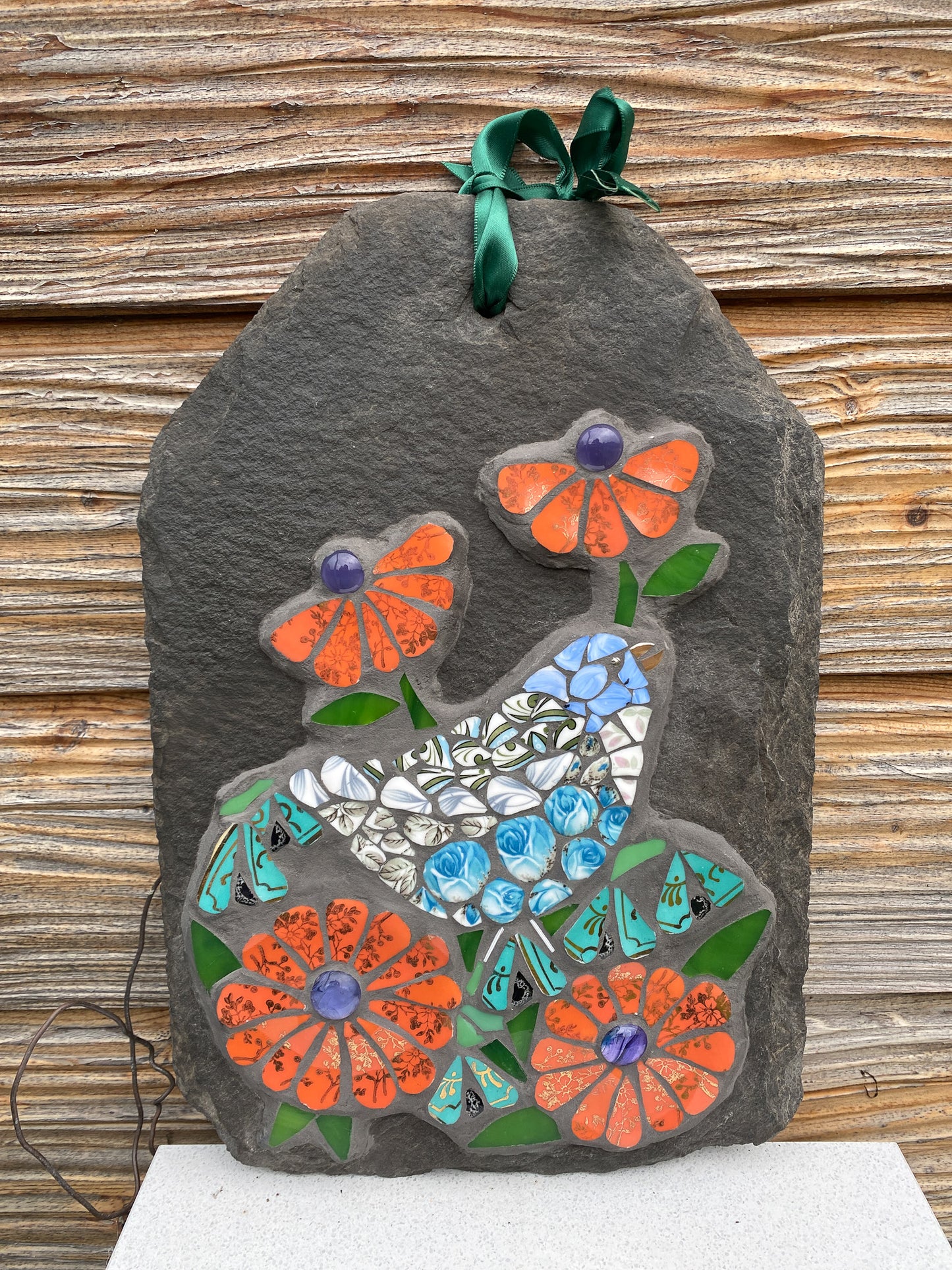 Decorative slate with mosaic flowers and bird design on a wooden background