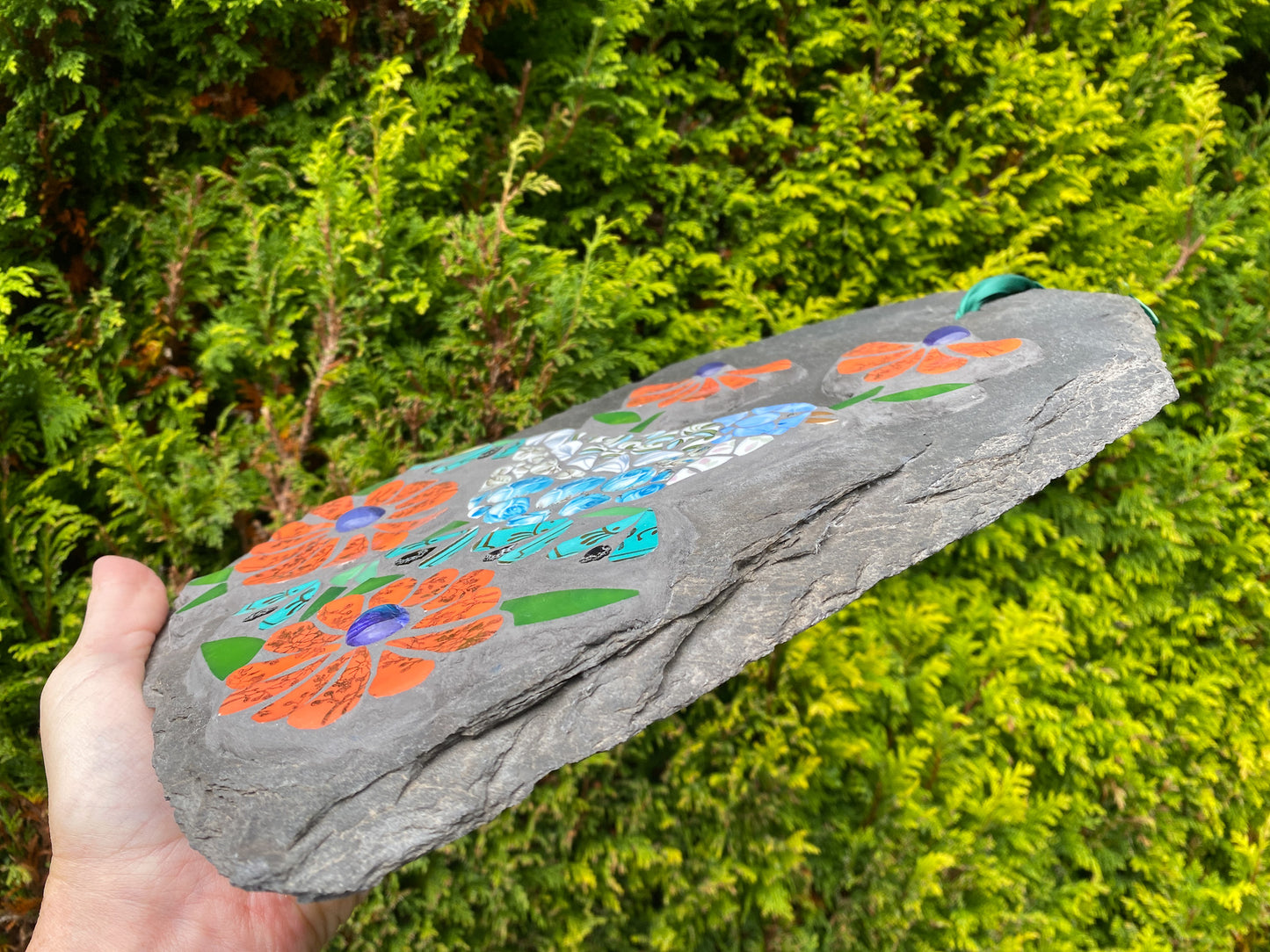 Decorative slate with floral designs held in front of green foliage
