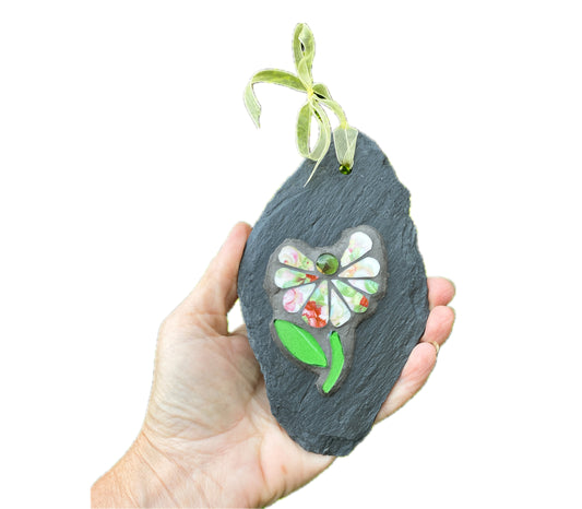 Hand holding a slate ornament with a floral design and ribbon on a white background