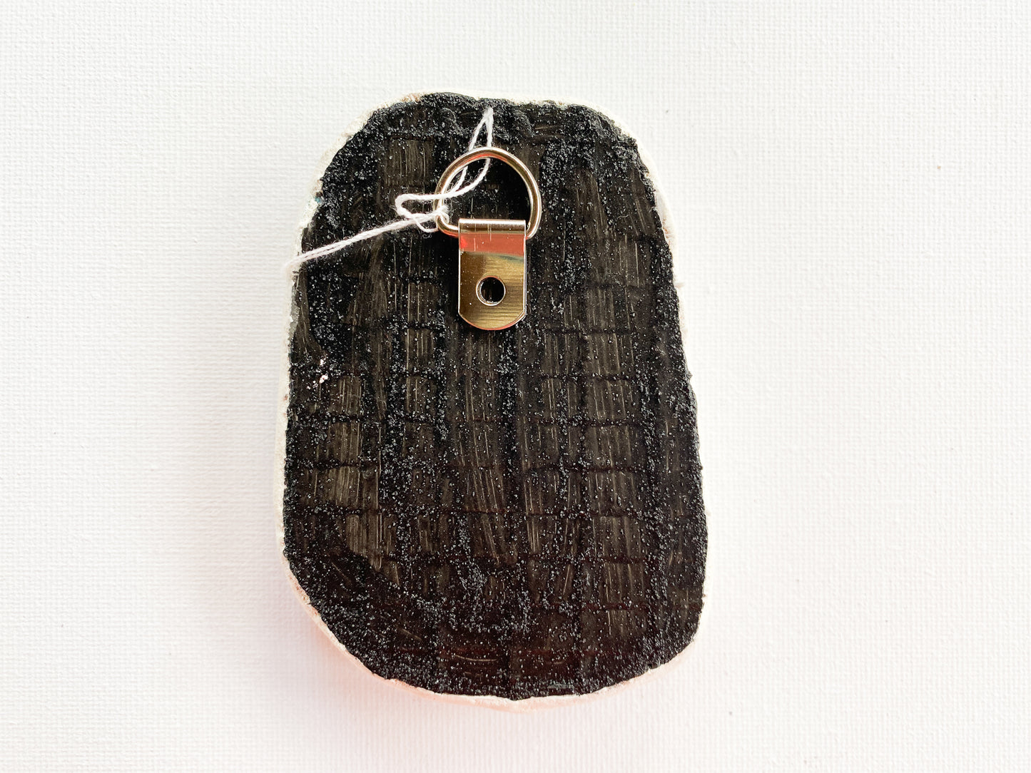 Black textured reverse side of mosaic with d-ringon a white background