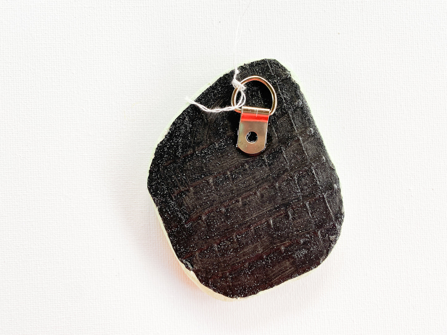 Black textured reverse side of mosaic with d-ring on a white background