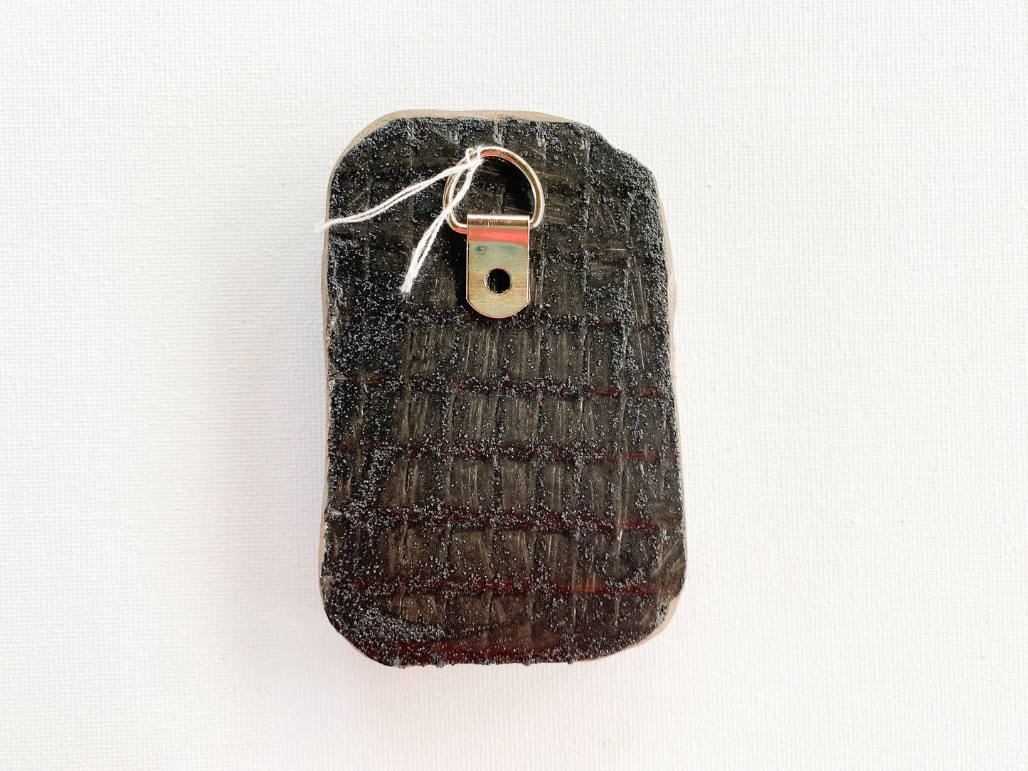 Textured black reverse side of mosaic with d-ring on a white background