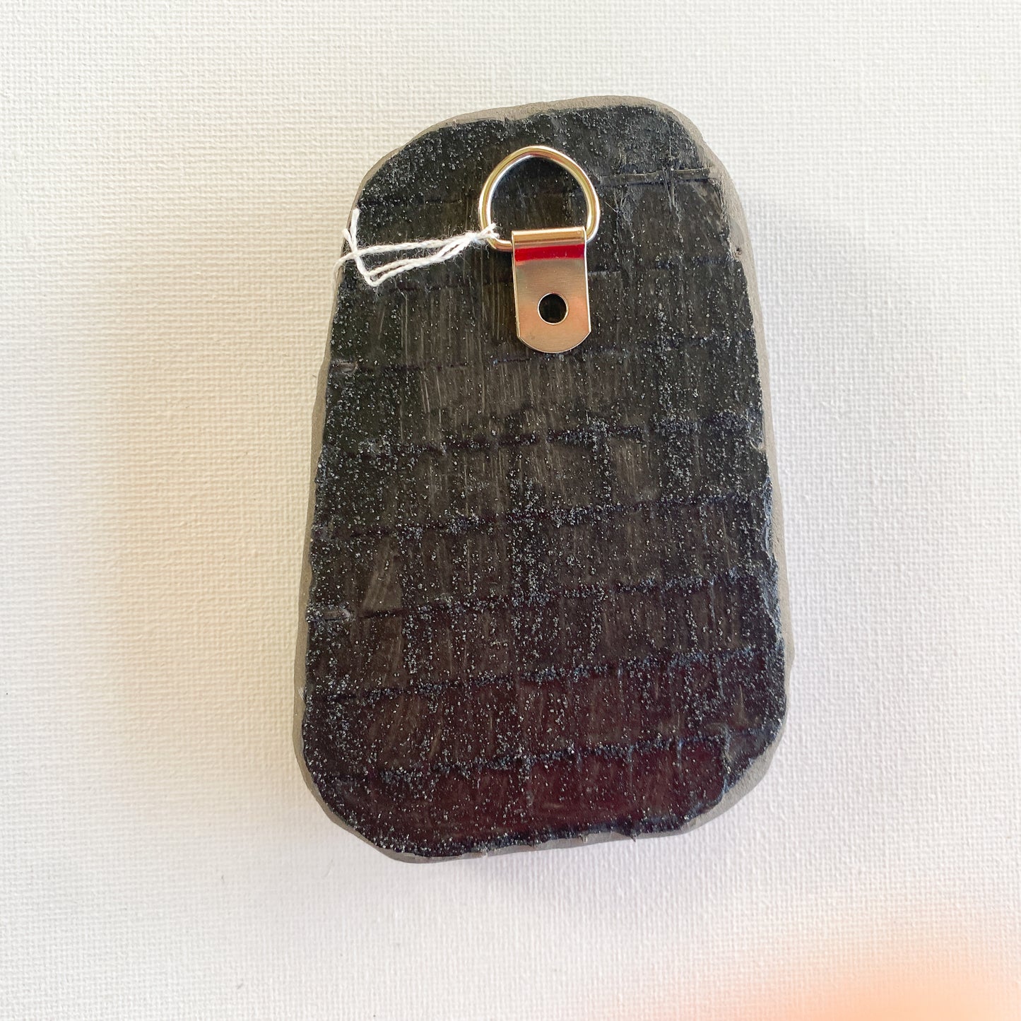 Black reverse side of a mosaic with a metal D-ring on a white background