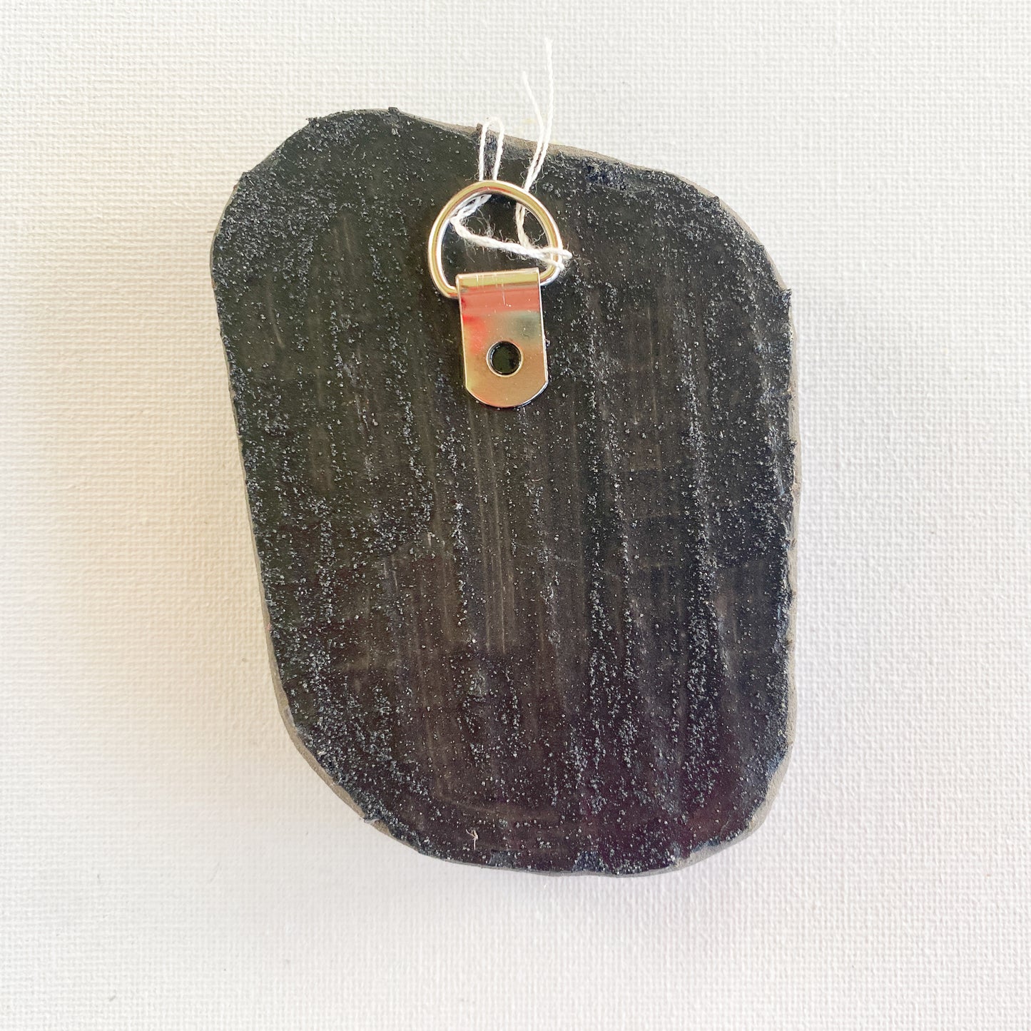 Black reverse side of a mosaic with a metal D-ring on a white background