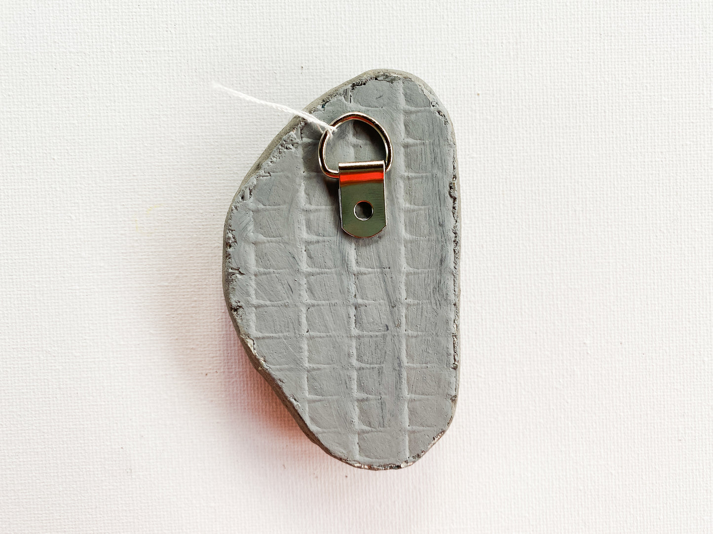 Gray textured reverse side of mosaic with d-ring on a white background