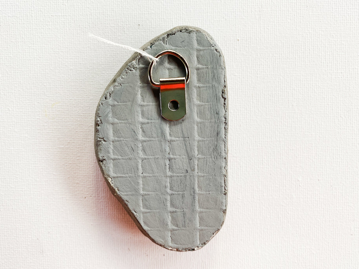 Gray textured reverse side of mosaic with d-ring on a white background