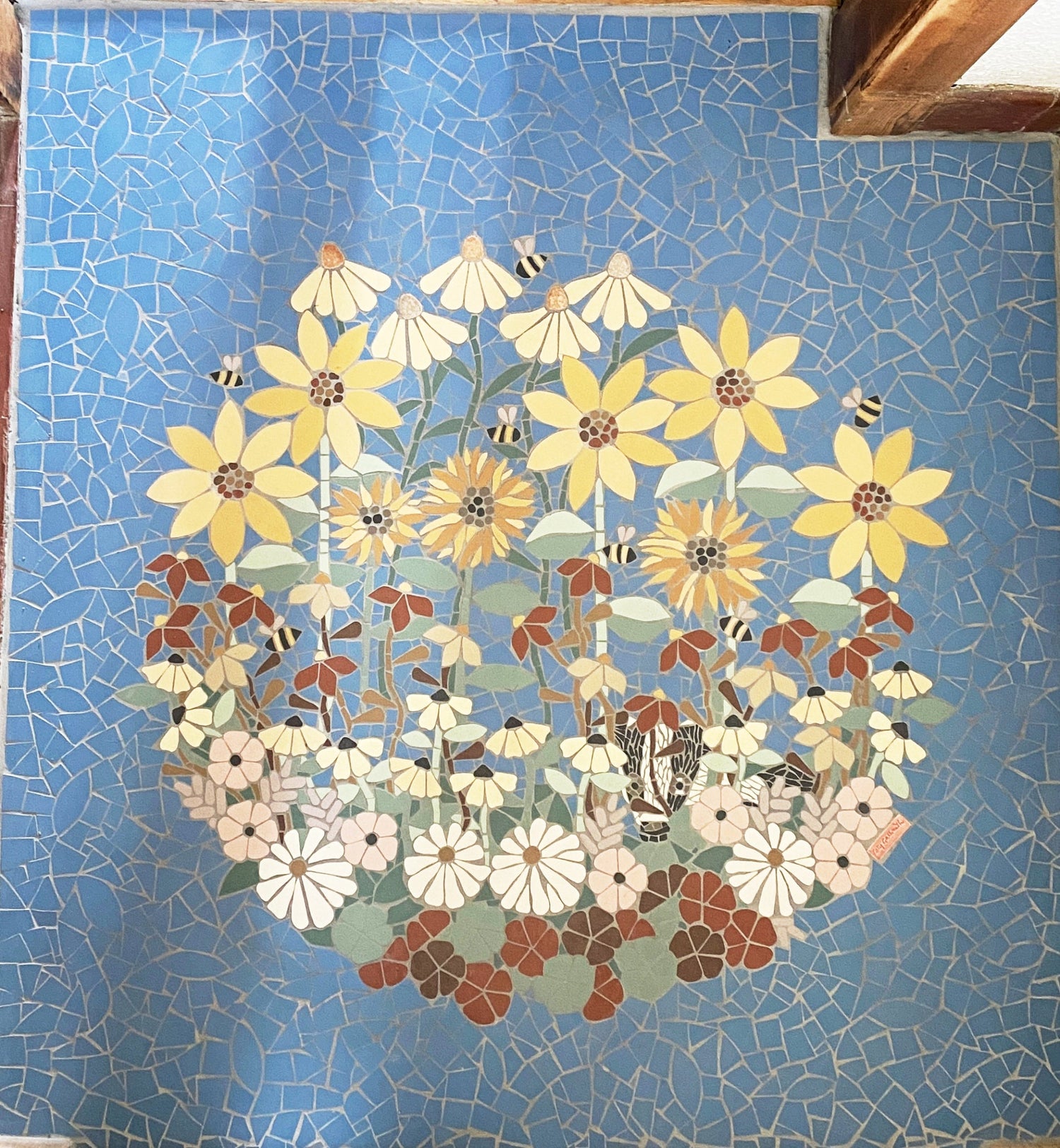 a round area of flowers with a badger peeking through, blue background, in mosaic