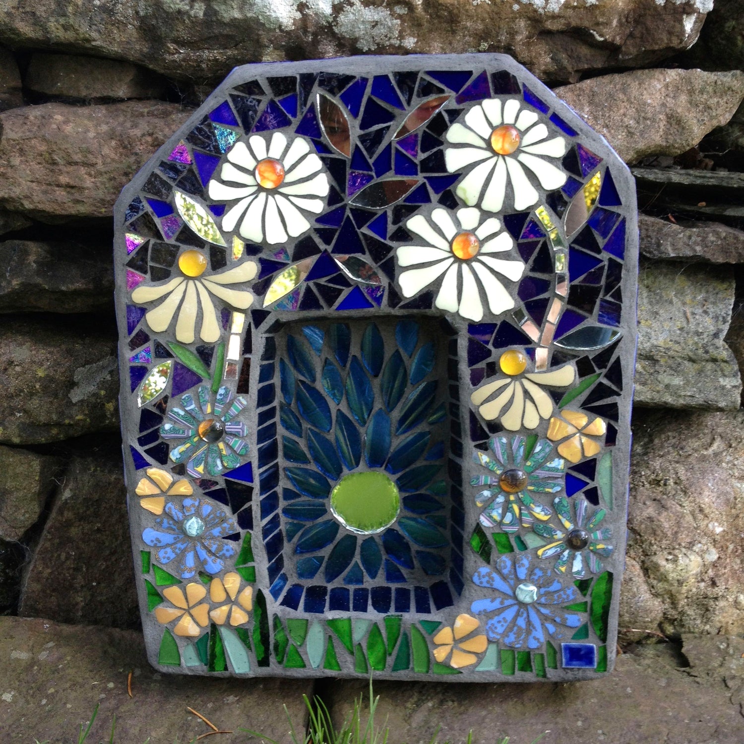 a small rectangular sculptural piece witha recess in the centre. it is decorated with flowers in mosaic