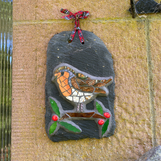 Decorative slate with a mosaic bird design hanging on a stone wall.