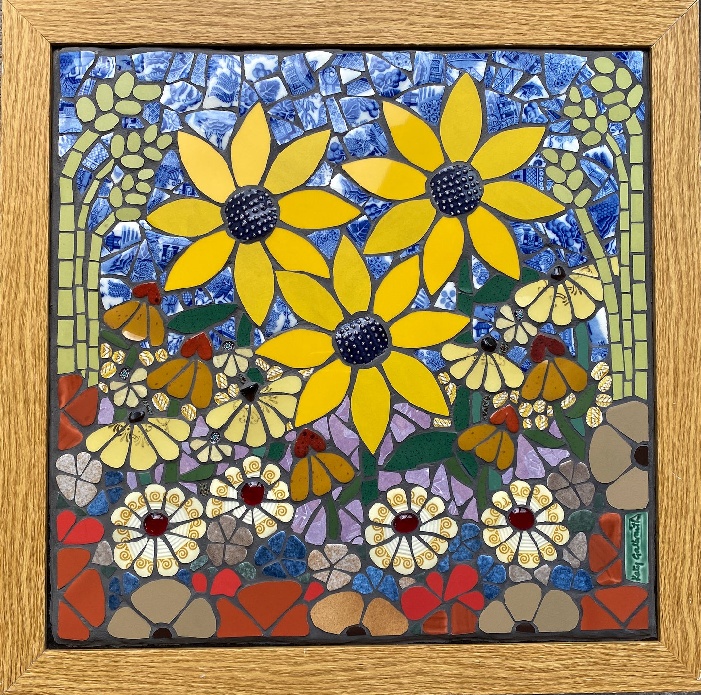 Mosaic artwork with yellow sunflowers, grasses and daisiy flowers and a wooden frame