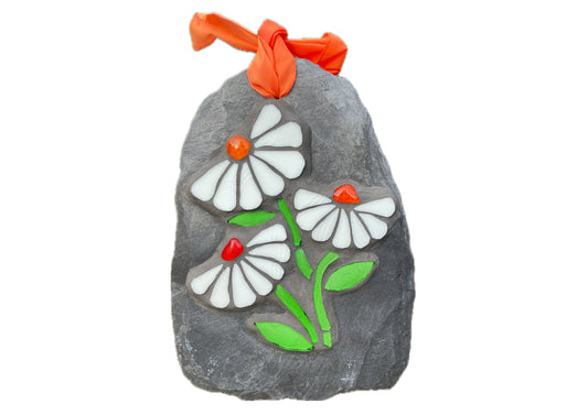 Three white daisies in mosaic on a grey slate.  Each daisy has seven petals and a vibrant orange nugget. bright green stem and leaves. on a white background