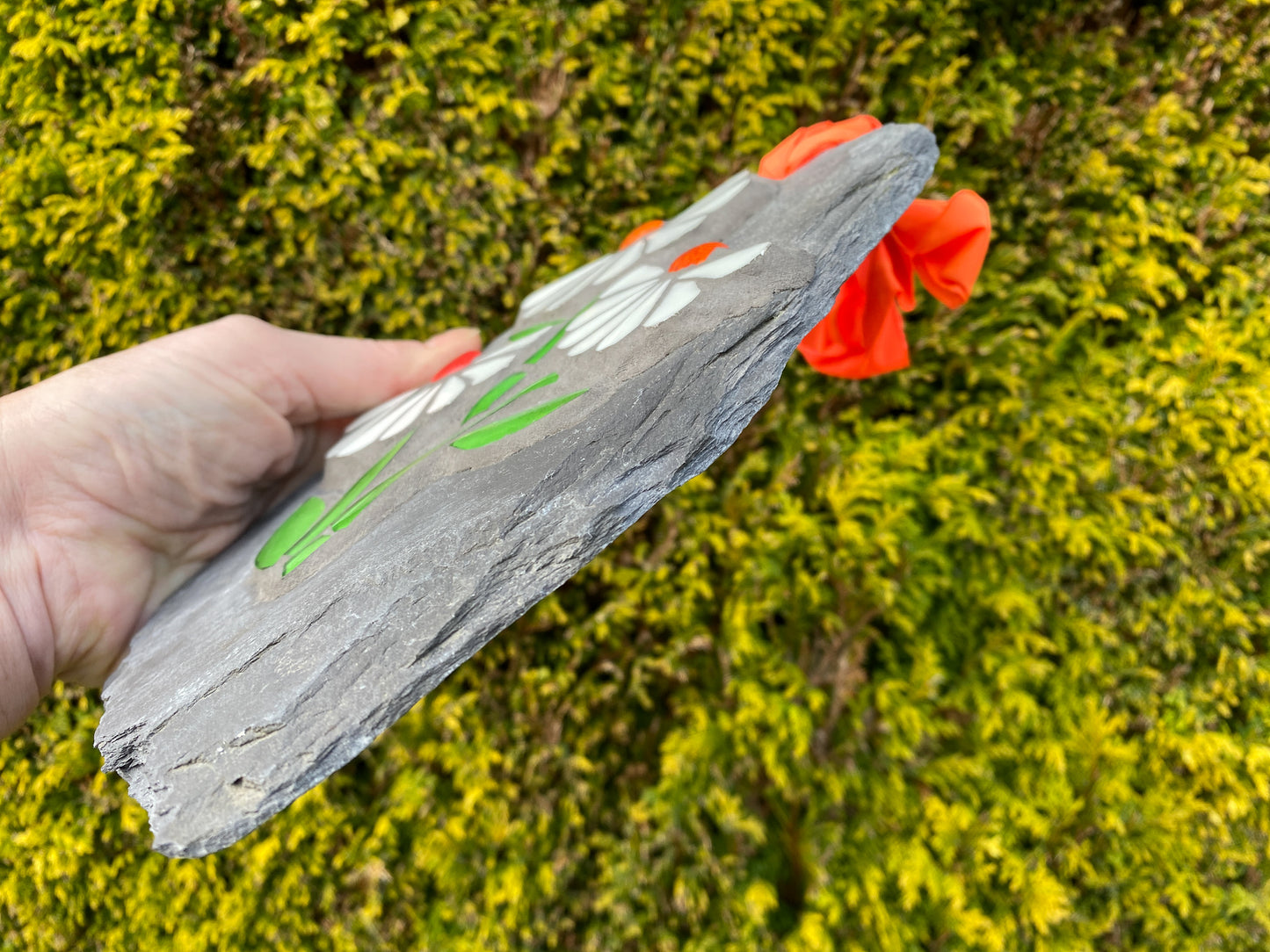 side view of a mosaic on slate, showing it's thickness. against an evergreen tree