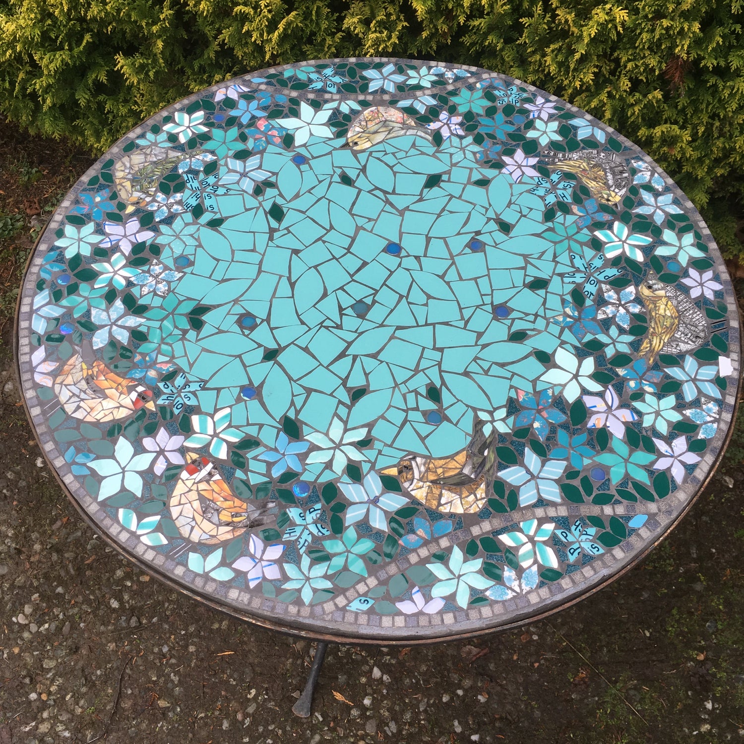 a circular mosaic tabletop with a variety of small birds in a garden, mostly in turquoise. made from recycled ceramic tiles and crockery. Made on commission