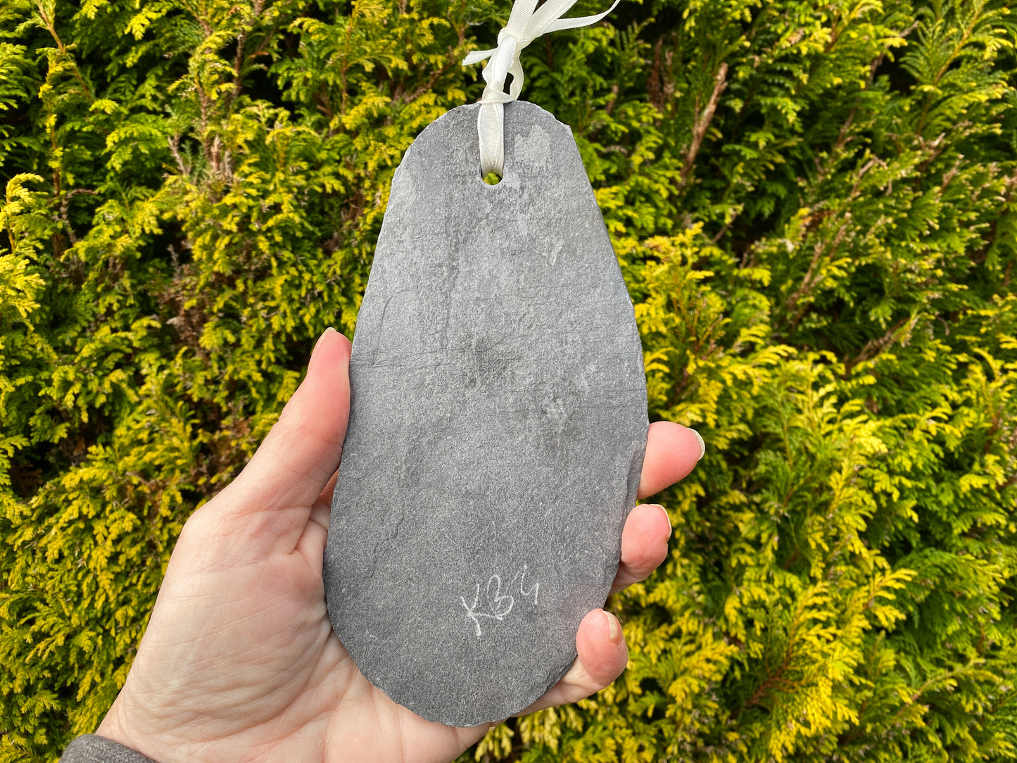 reverse of a grey slate, showing a hole with white ribbon through, and artist signature