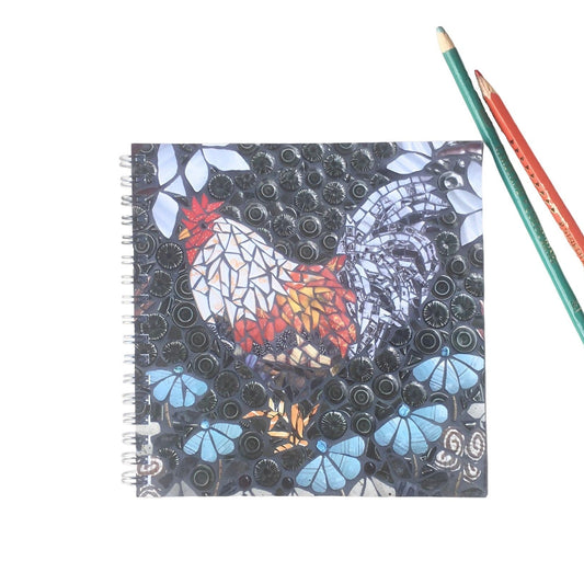 spiral bound notebook and two pencils on a white background.  the image on the front of the notebook is of a chicken in mosaic