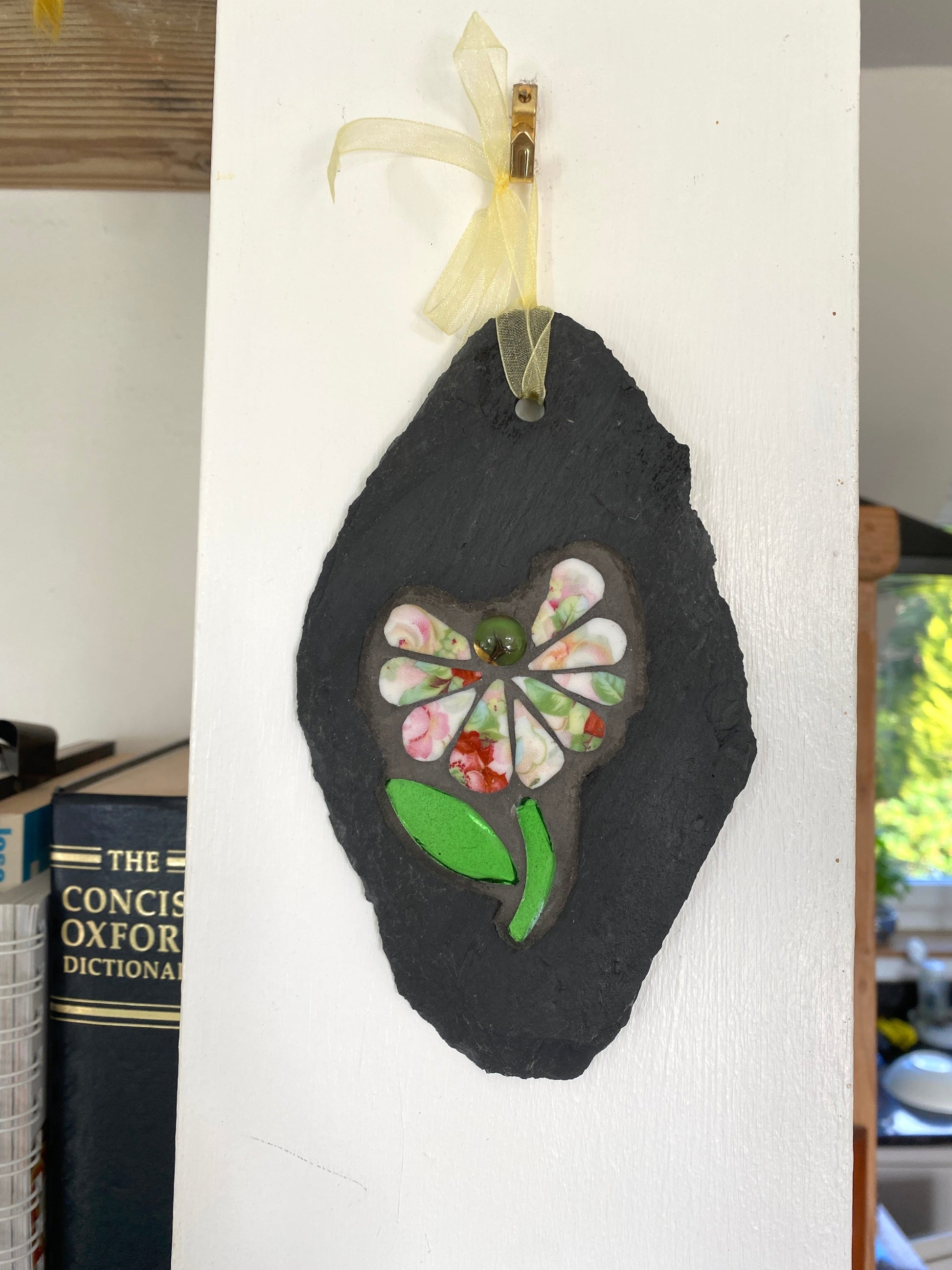 Decorative slate with a floral mosaic design hanging on a white wall.