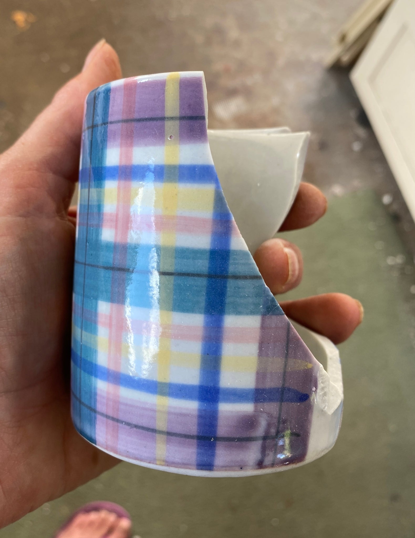 Hand holding a broken mug with a tartan-pattern with a blurred background