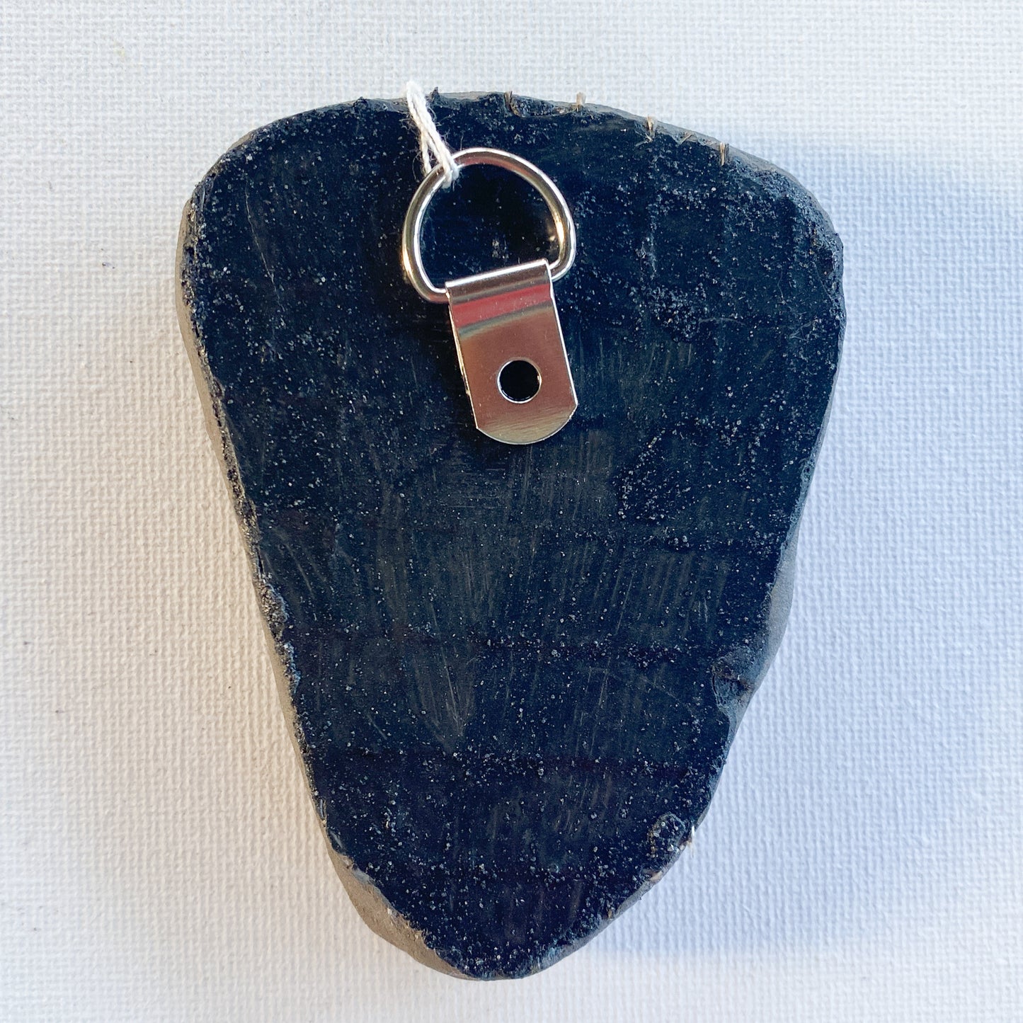 Black reverse side of a mosaic with a metal D-ring on a white background