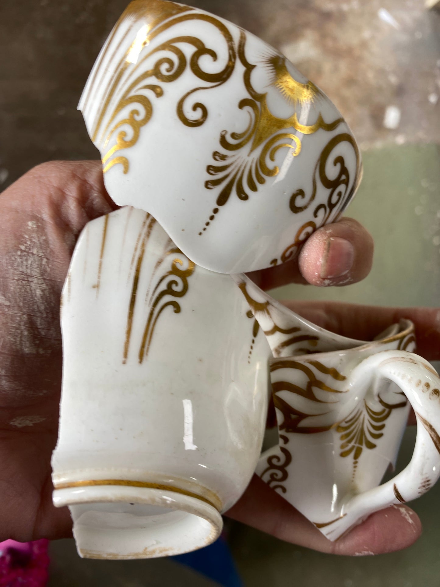 Broken white ceramic jug with gold decorative patterns held by a hand.