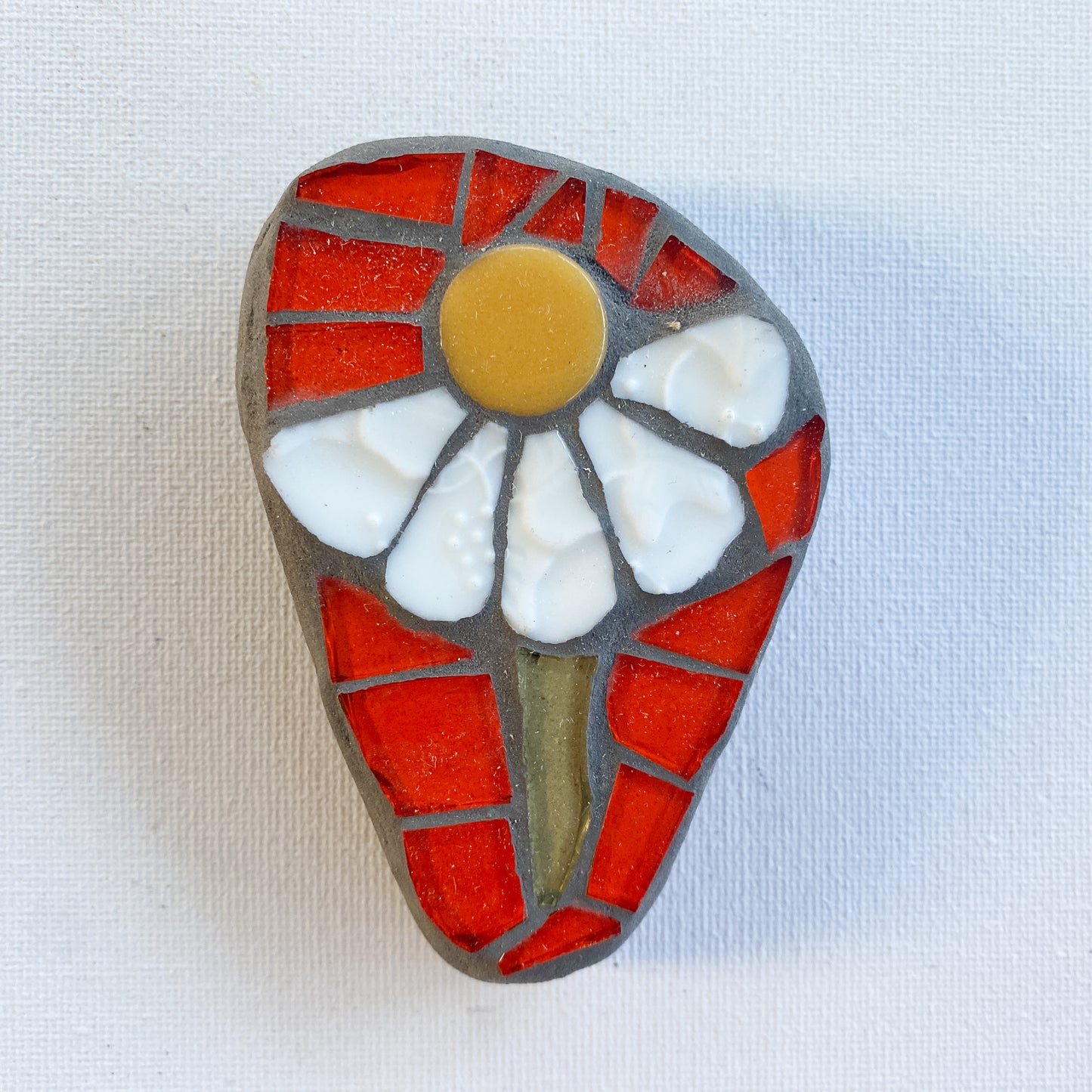 Mosaic art piece with a white flower design on an orange background photographed on white