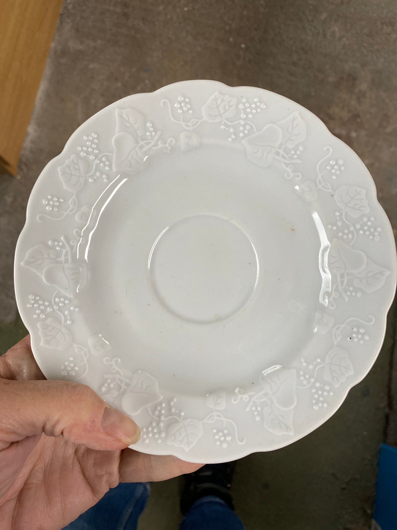White decorative plate held by a hand on a concrete floor.