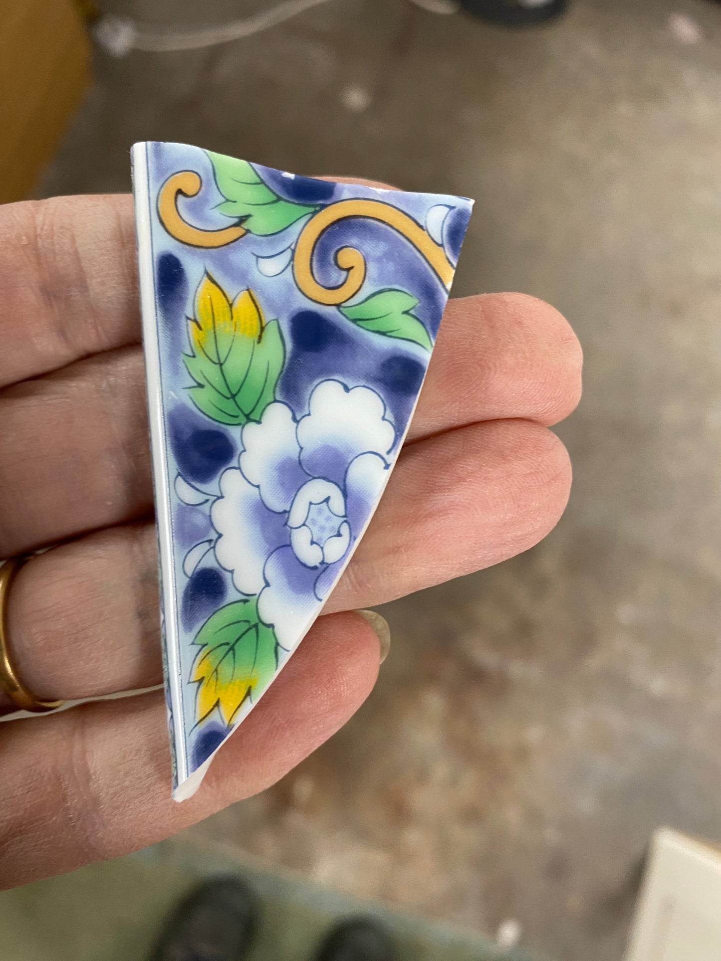 Hand holding a triangular ceramic tile with floral design