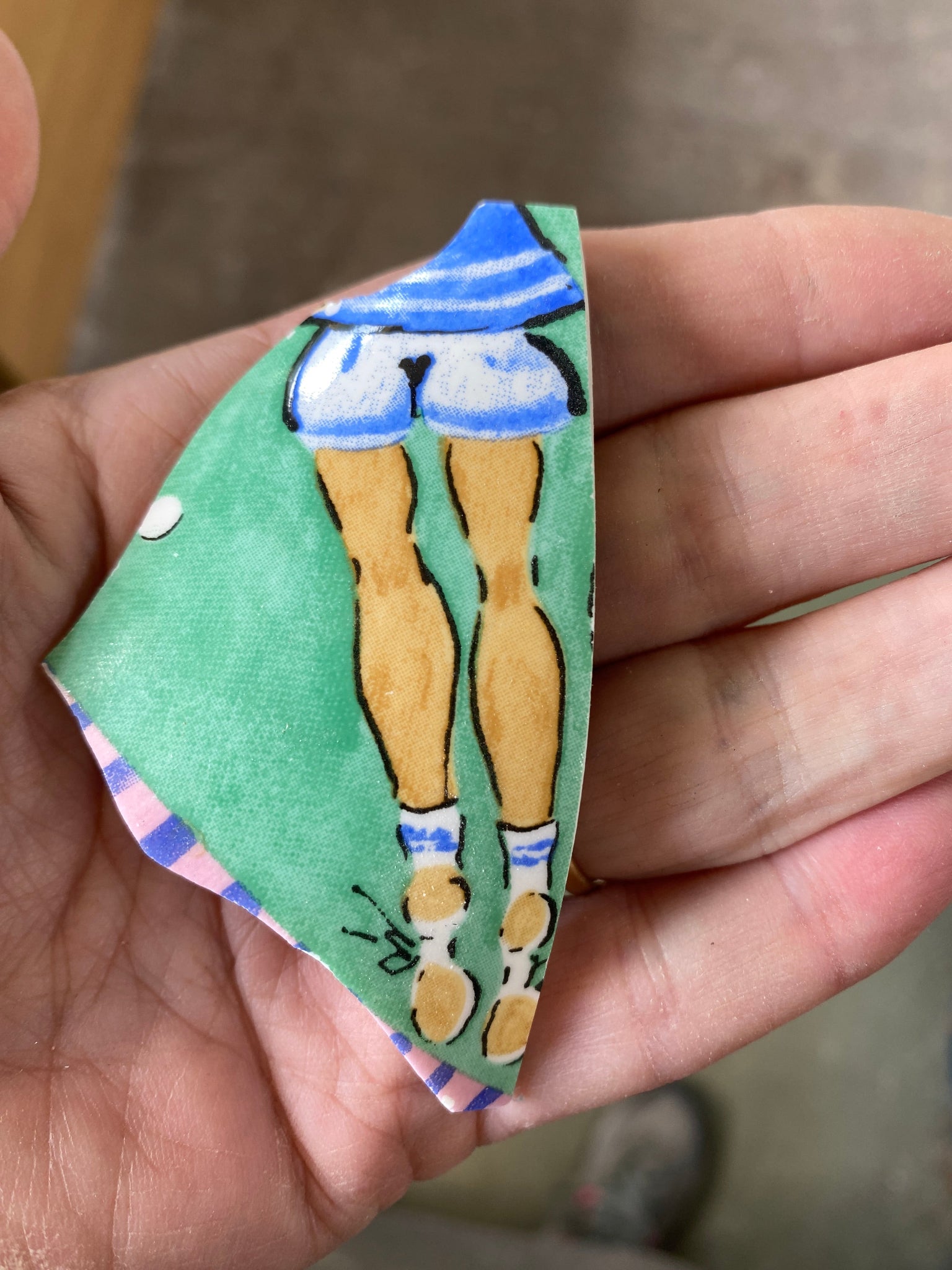 Hand holding a triangular piece of ceramic with a pair of leg design on a blurred background