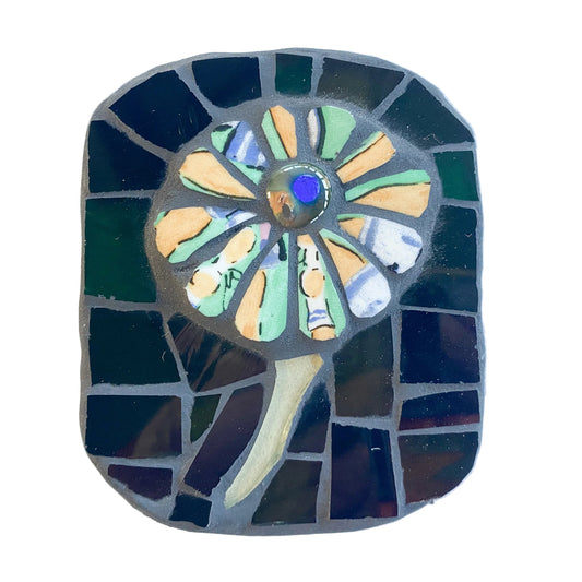 Mosaic art piece with a cream and green flower design on a dark background photographed on white