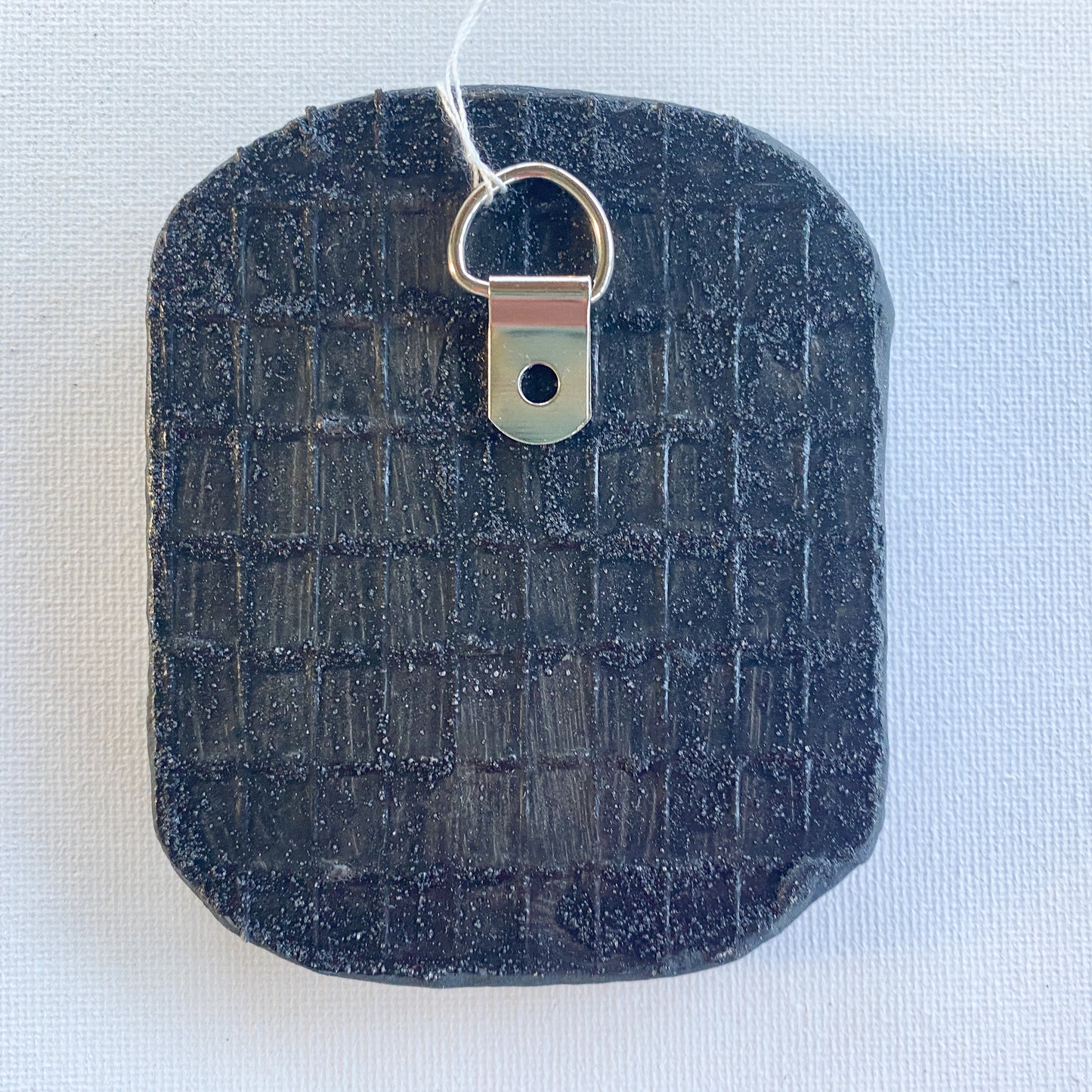 Black reverse side of a mosaic with a metal D-ring on a white background