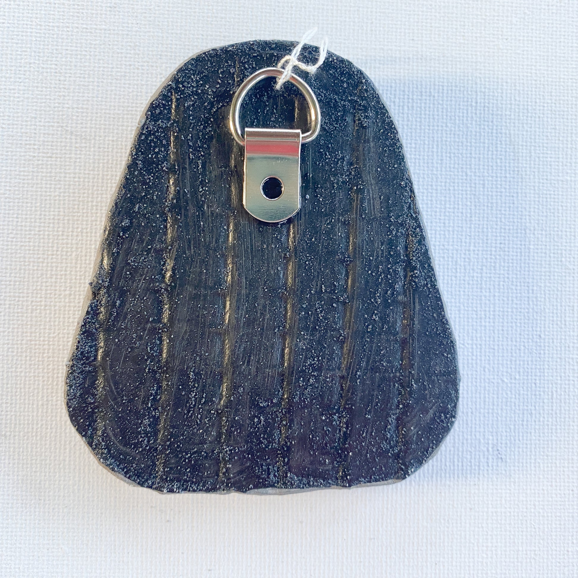 Black reverse side of a mosaic with a metal D-ring on a white background