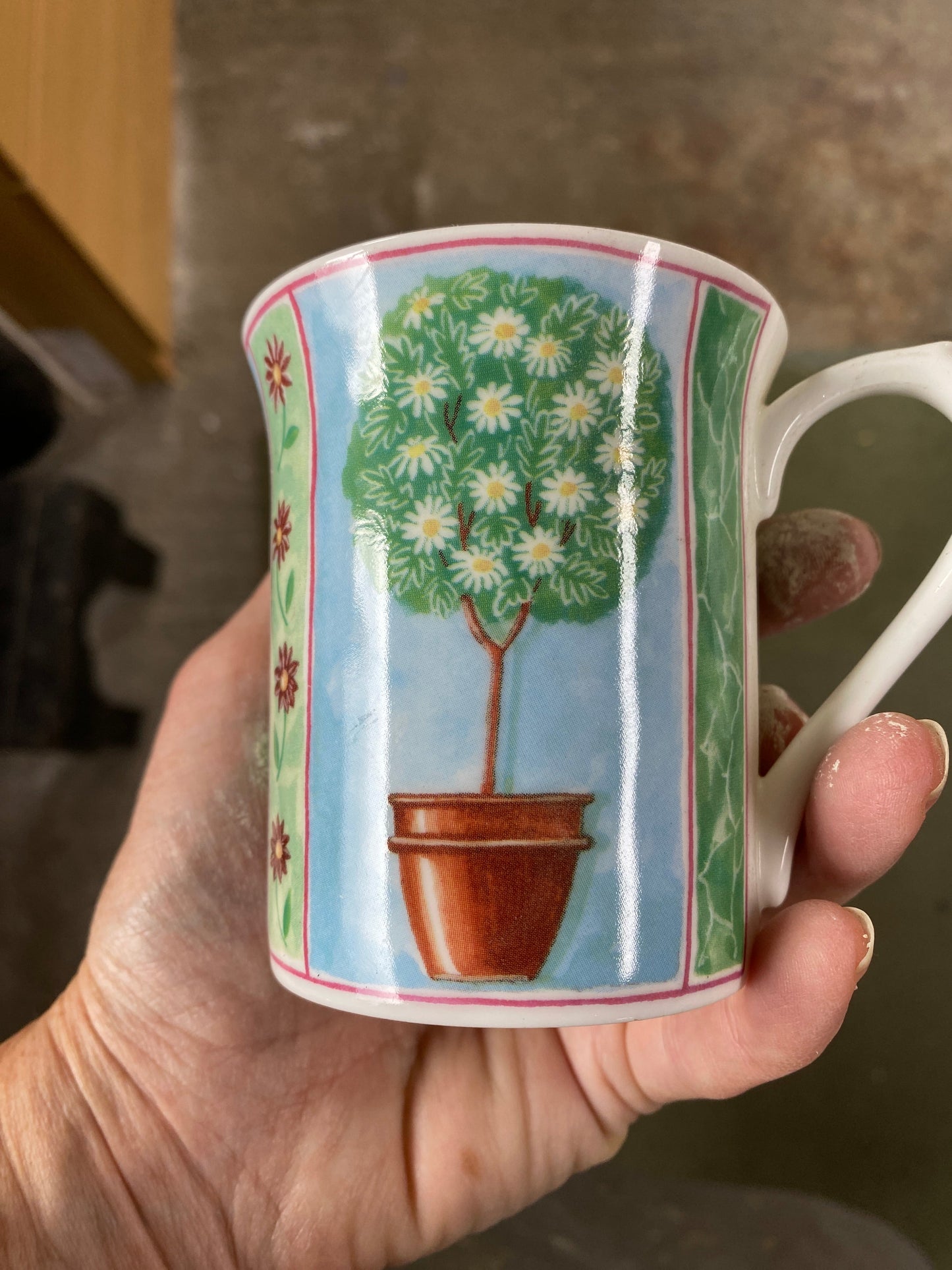 Hand holding a mug with a scenic design of a tree and house.