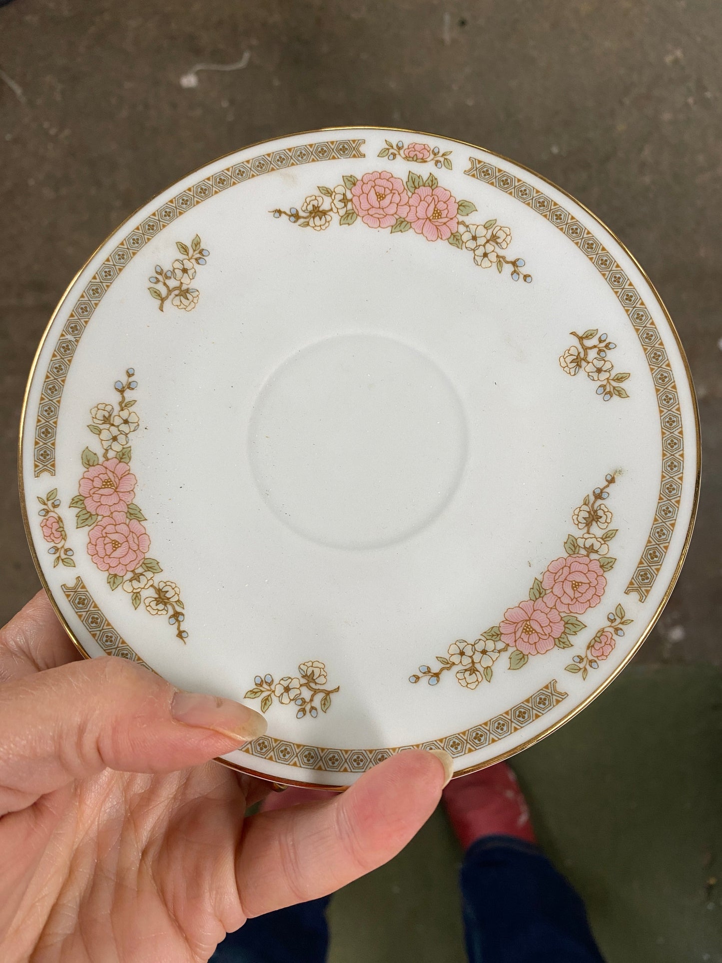 Decorative saucer with floral patterns held by a hand on a concrete surface