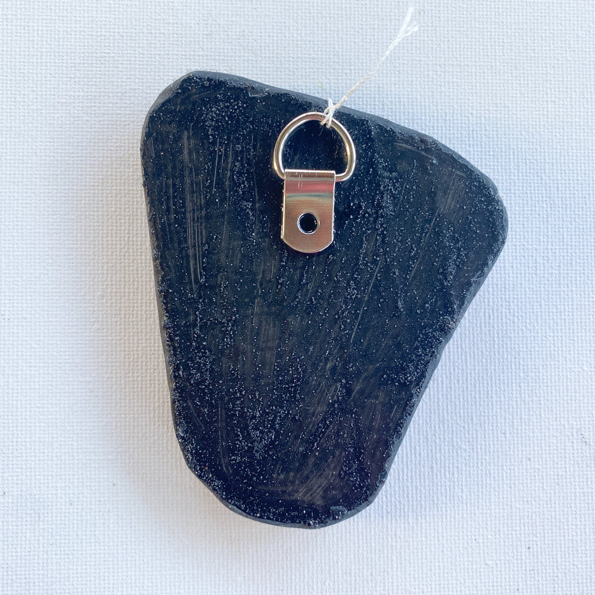 Black reverse side of a mosaic with a metal D-ring on a white background