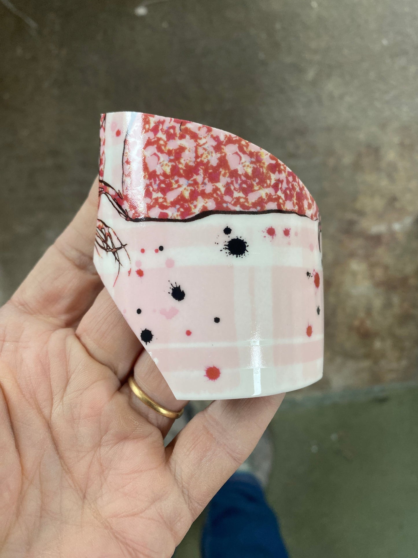 Hand holding a folded piece of ceramic mug with floral pattern against a blurred background