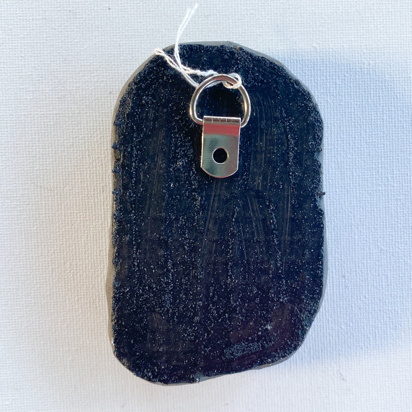 Black reverse side of a mosaic with a metal D-ring on a white background