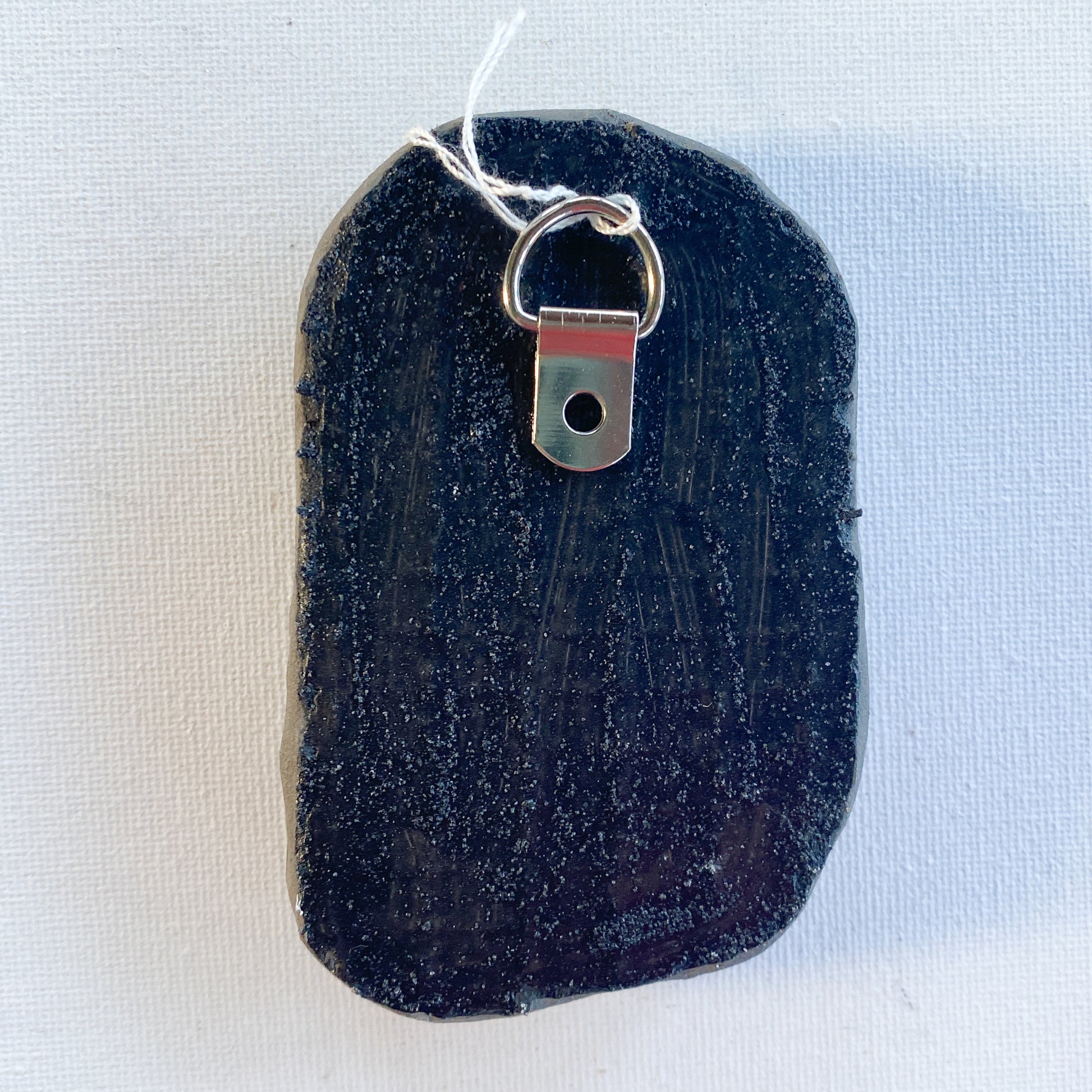 Black reverse side of a mosaic with a metal D-ring on a white background