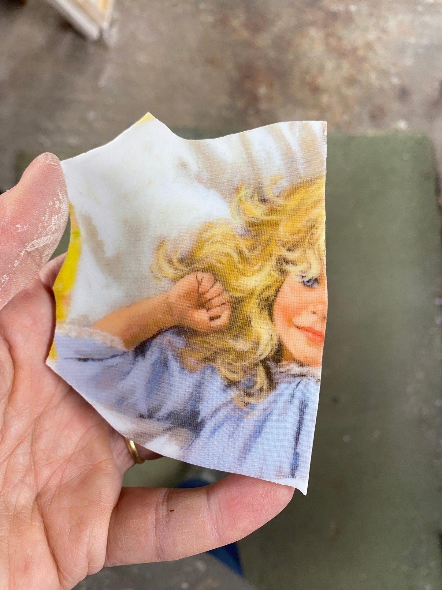 Hand holding a small ceramic shard with printed image of a child with blonde hair.
