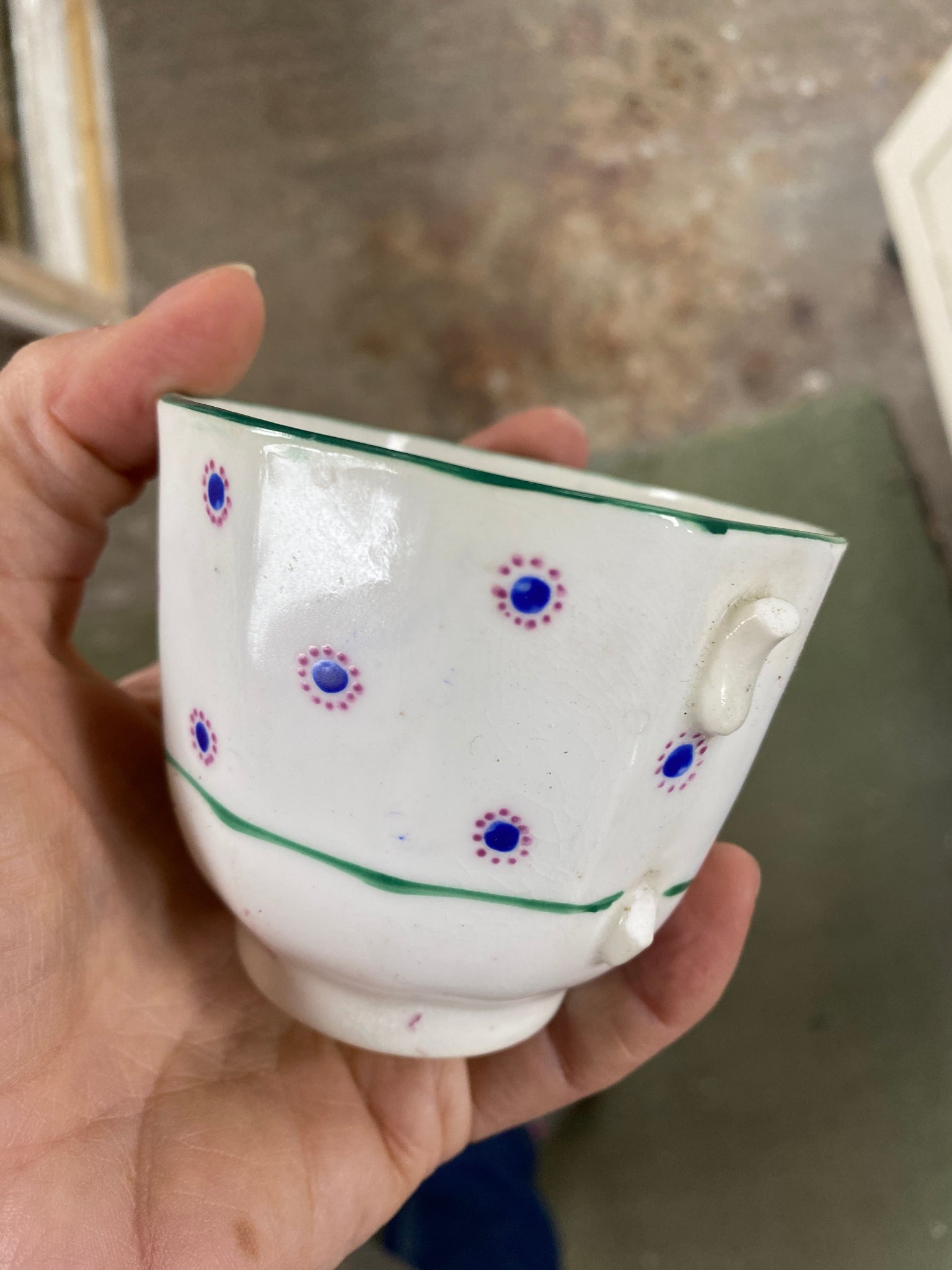 Hand holding a ceramic teacup with decorative patterns on a blurred background